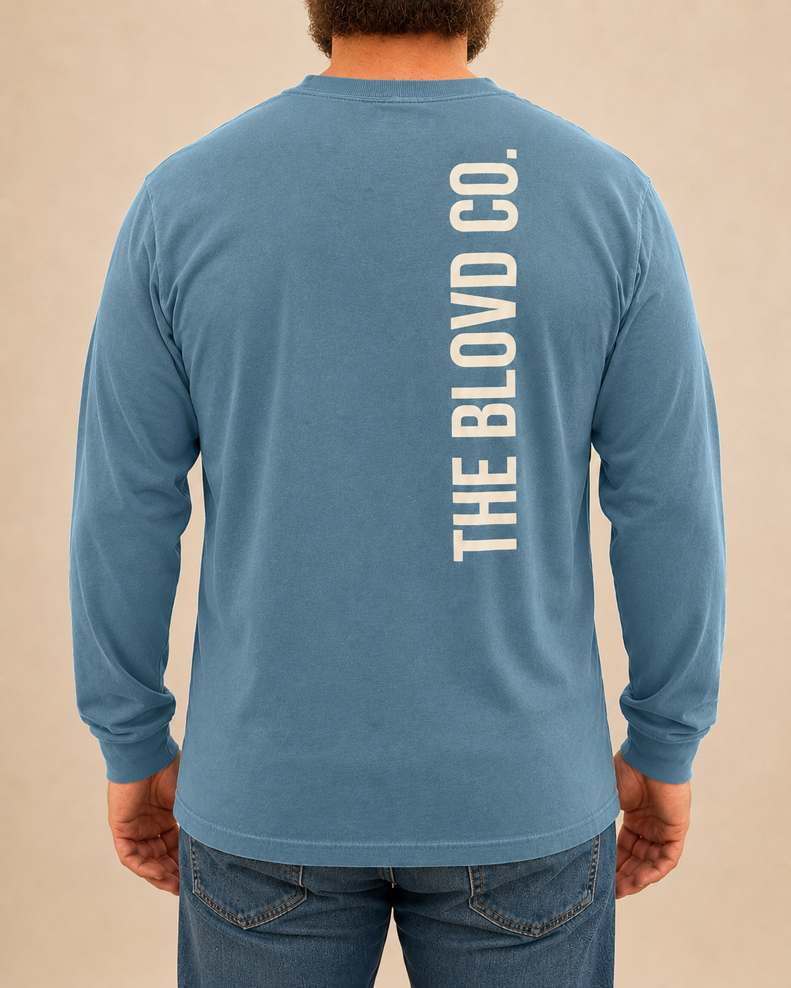 THE BLOVD Lion Signature Comfort Colors 6014 Blue Jean long sleeve with Warm Ivory vertical THE BLOVD CO. back wordmark, approved male rear studio view