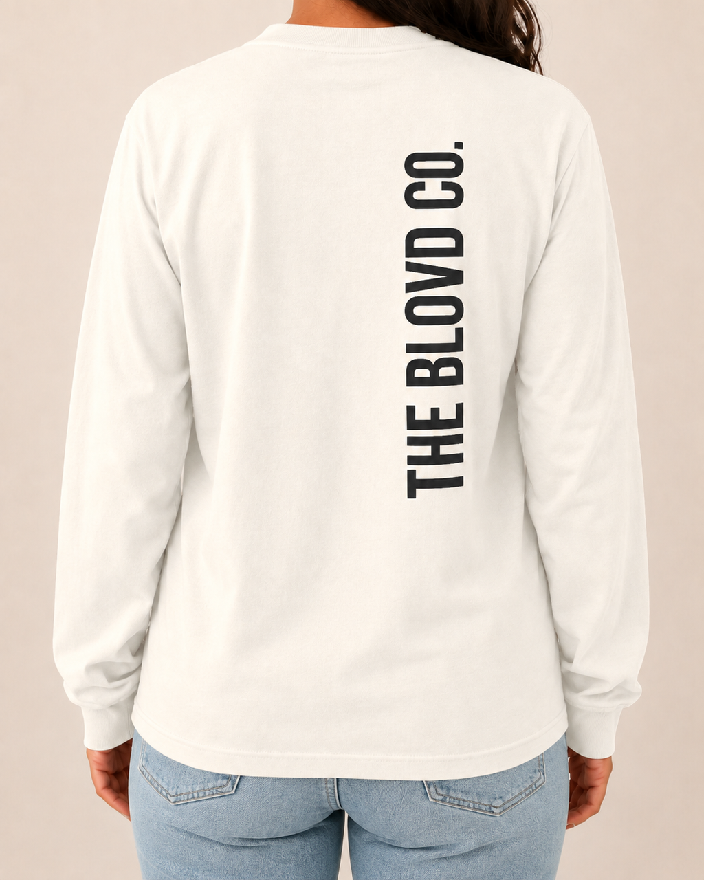 THE BLOVD Lion Signature Comfort Colors 6014 Ivory long sleeve with Deep Charcoal vertical THE BLOVD CO. back wordmark, approved female rear studio view with jeans