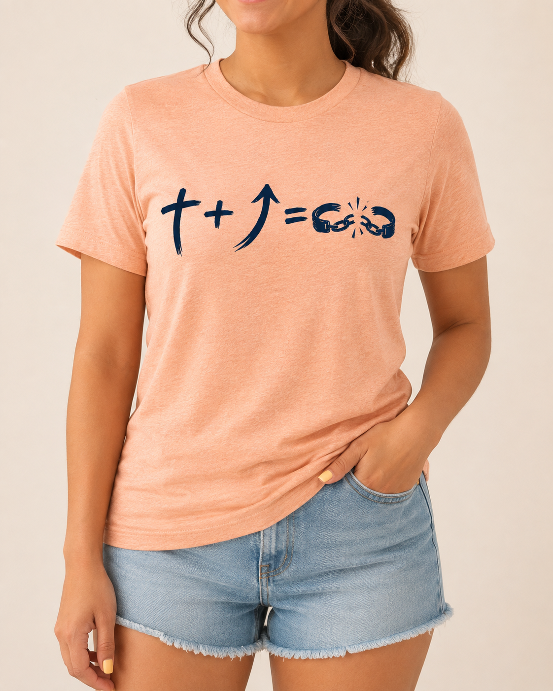 Freedom Galatians 5:1 Bella+Canvas Heather Peach tee with BLOVD Heritage Navy artwork, approved female warm-neutral studio front view cropped below the lips with denim shorts visible.
