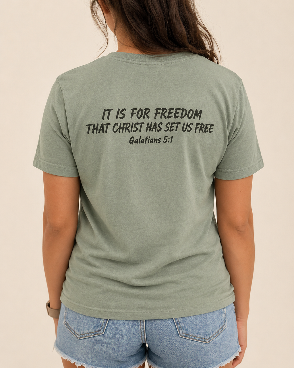 Freedom Galatians 5:1 Bella+Canvas Sage tee with BLOVD Weathered Espresso Scripture artwork, approved female warm-neutral studio back view showing the back of the neck with denim shorts visible.