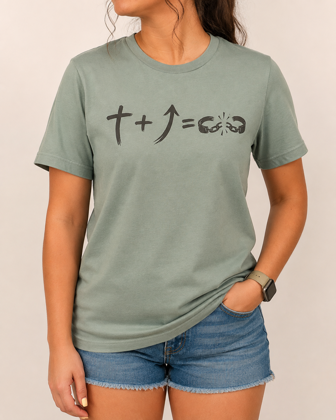 Freedom Galatians 5:1 Bella+Canvas Sage tee with BLOVD Weathered Espresso artwork, approved female warm-neutral studio front view cropped below the lips with denim shorts visible.