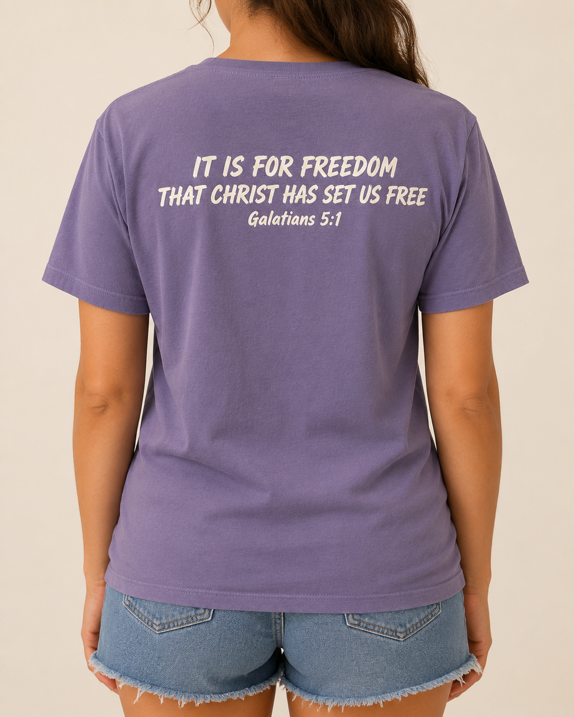 Freedom Galatians 5:1 Comfort Colors Violet tee with BLOVD Antique Bone Scripture artwork, approved female warm-neutral studio back view showing the back of the neck with denim shorts visible.